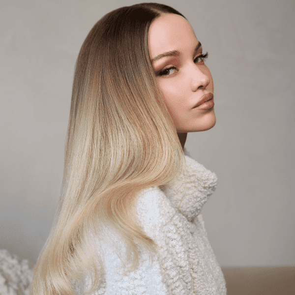 Dove Cameron posing in a cream colored knit sweater to showcase her blonde transformation with Schwarzkopf Professional®, with shadow roots and lighter ends.