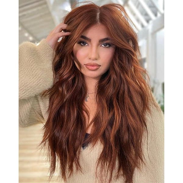 Woman with long wavy hair in trendy cowboy copper color, wearing a cozy beige sweater indoors.