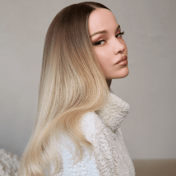 Dove Cameron posing in a cream colored knit sweater to showcase her blonde transformation with Schwarzkopf Professional®, with shadow roots and lighter ends.