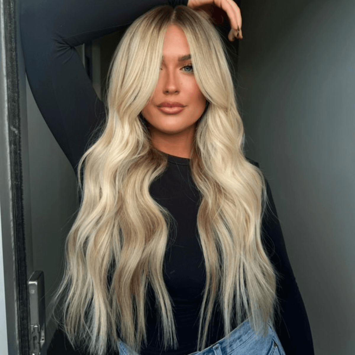 Client with long, wavy blonde Slavic extensions styled with curtain bangs and dimensional color for a seamless finish