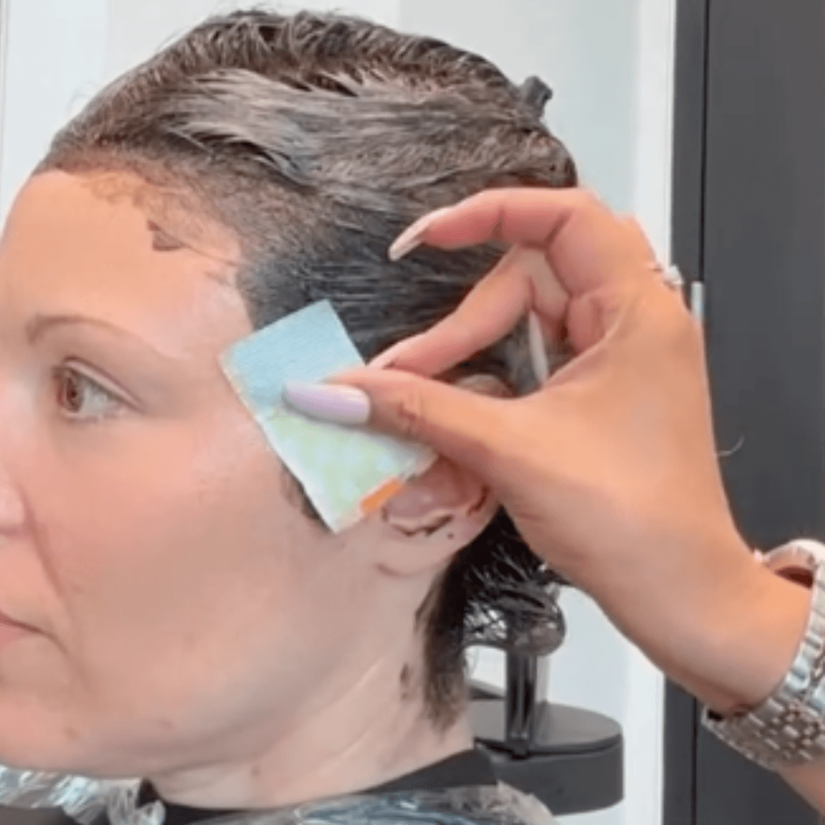hand placing small foil rectangle on hairline near ear with all over color applied