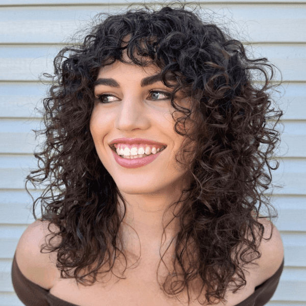 Smiling woman with dark, curly hair featuring layered styling and face-framing fringe, showcasing a low-maintenance haircut for natural curls.