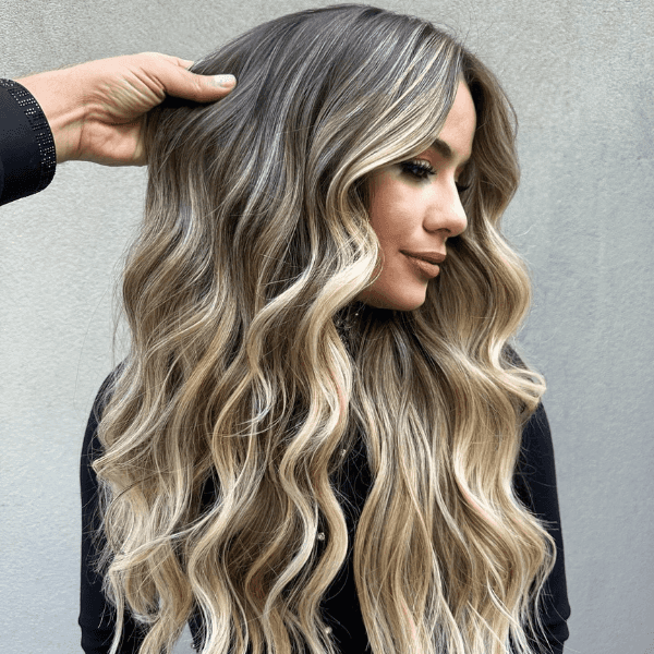 Long wavy blonde balayage hairstyle with soft highlights, styled by Gabriel Samra, showcasing natural beachy waves and multi-dimensional color.
