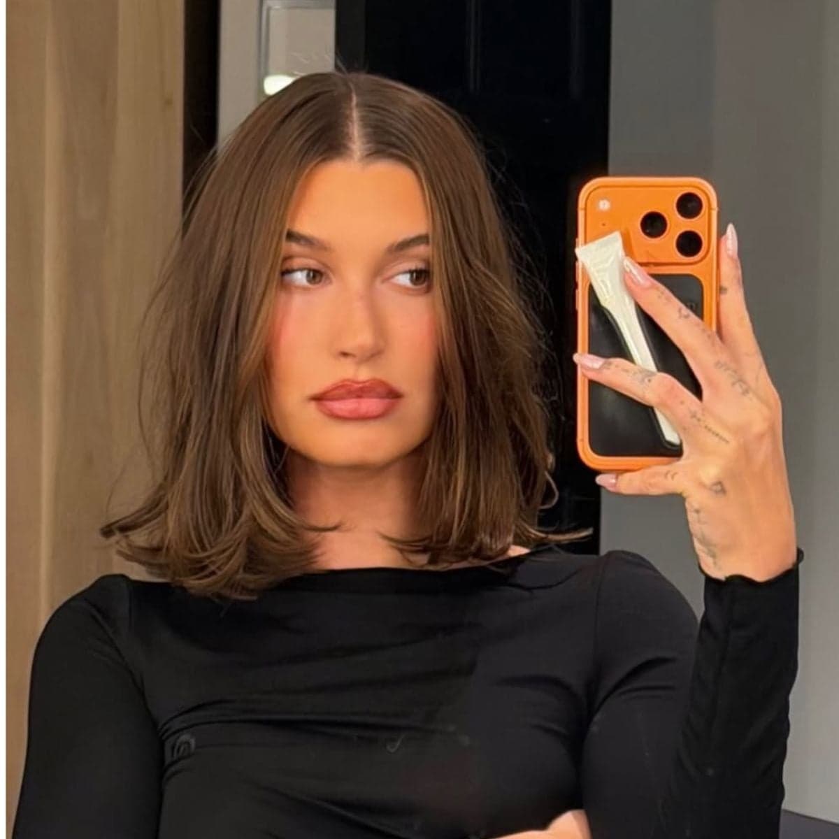 Hailey Bieber taking a mirror selfie showing a shoulder-skimming blunt lob haircut with a center part and soft face-framing layers.