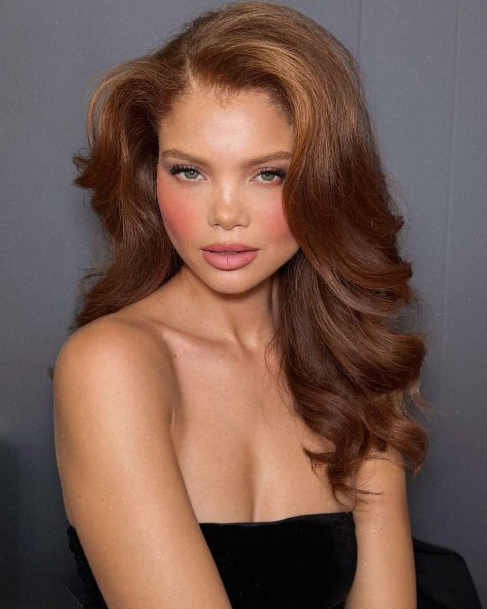 Model with long copper hair styled in soft, voluminous layers and face-framing movement.
