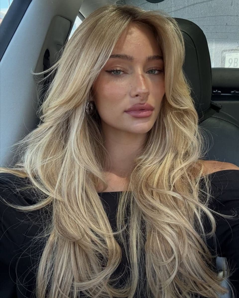 Blonde model with long, layered hair extensions styled with soft face-framing layers and voluminous waves.