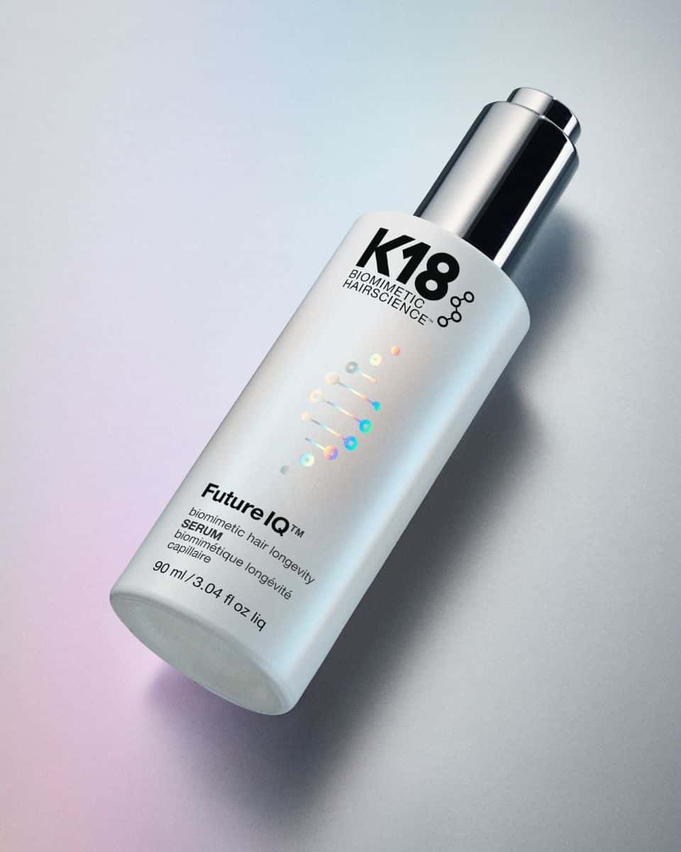 K18 FutureIQ Biomimetic Hair Longevity Serum bottle photographed against a softly lit silver background with iridescent pink and blue tones.