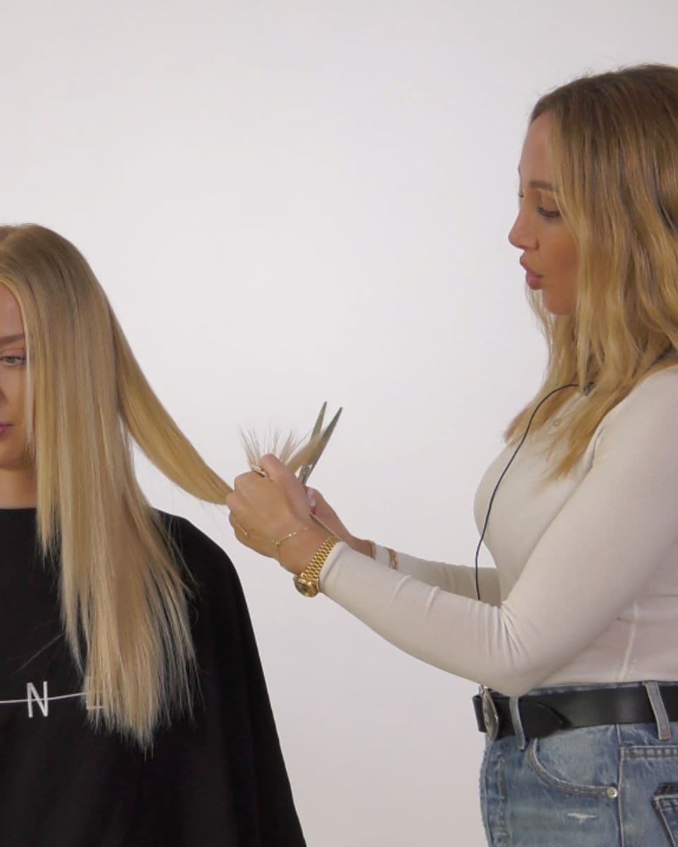 Stylist point cuts the ends of blonde hair extensions to remove bulk and create a softer, more blended finish.