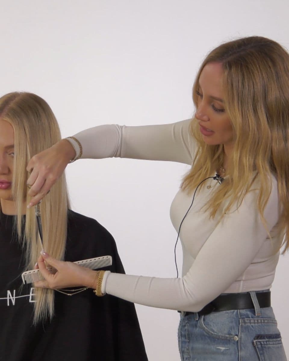 Stylist demonstrates slide cutting on blonde hair extensions to soften weight and create seamless face-framing layers.